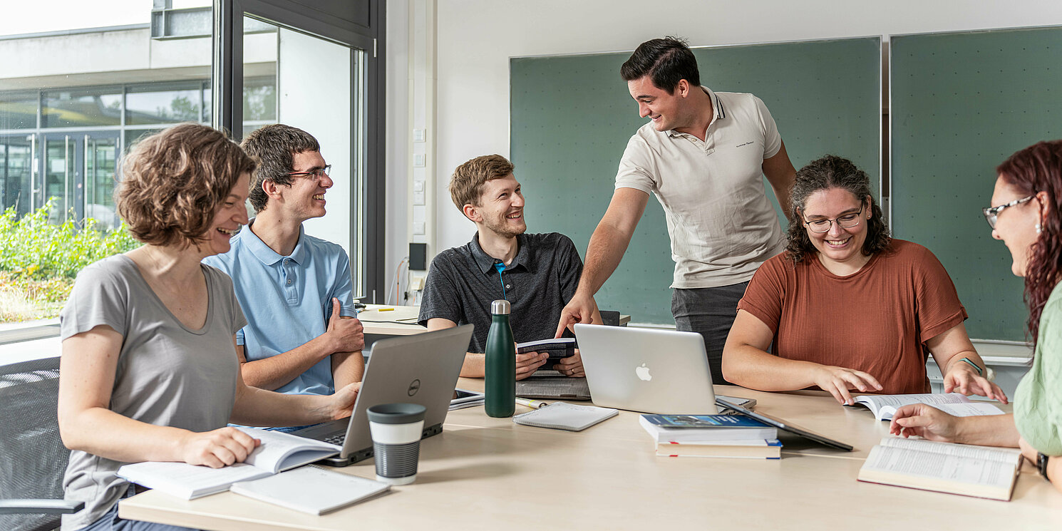 Hochschulzertifikat Future Skills for Business Professionals berufsbegleitend absolvieren Studierende arbeiten in einer Lerngruppe mit Laptops und Unterlagen an einem großen Tisch.