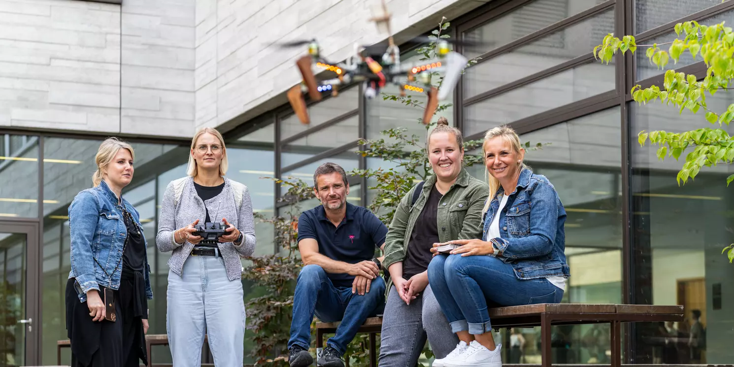 Systemtechnik berufsbegleitend studieren Studierende stehen in einem Innenhof und eine Studentin steuert eine fliegende Drohne.