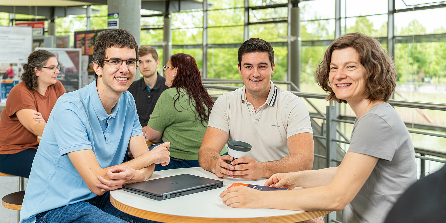 Zentrum für Weiterbildung und Wissensmanagement Studierende sitzen an einem Tisch in der Cafeteria und unterhalten sich.