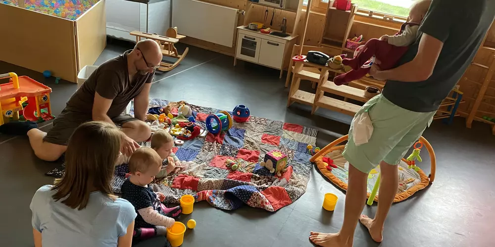 Parents play with their children on a colorful blanket.