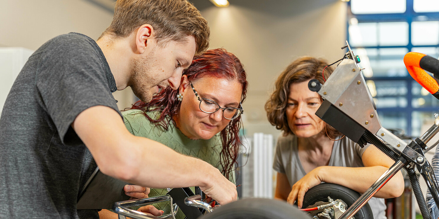 Zentrum für Weiterbildung und Wissensmanagement Drei Studierende arbeiten an einem Fahrzeug.